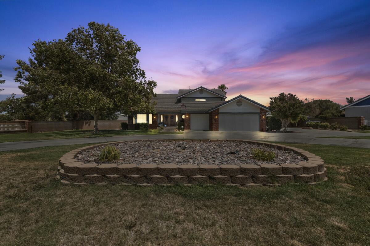 A large two-story home with trees around it and a large rock-filled round stone decoration in the front