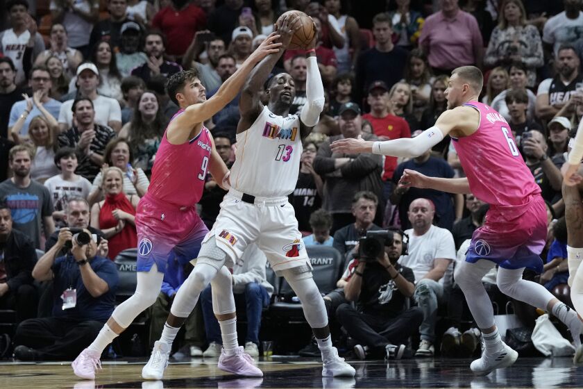 El centro de los Heat de Miami Bam Adebayo (13) busca un espacio antes de tirar frente a sus rivales de los Wizards de Washington, el delantero Deni Avdija (9) y el centro Kristaps Porzingis (6), durante la primera mitad de su partido de la NBA el viernes 25 de noviembre de 2022, en Miami. (AP Foto/Wilfredo Lee)