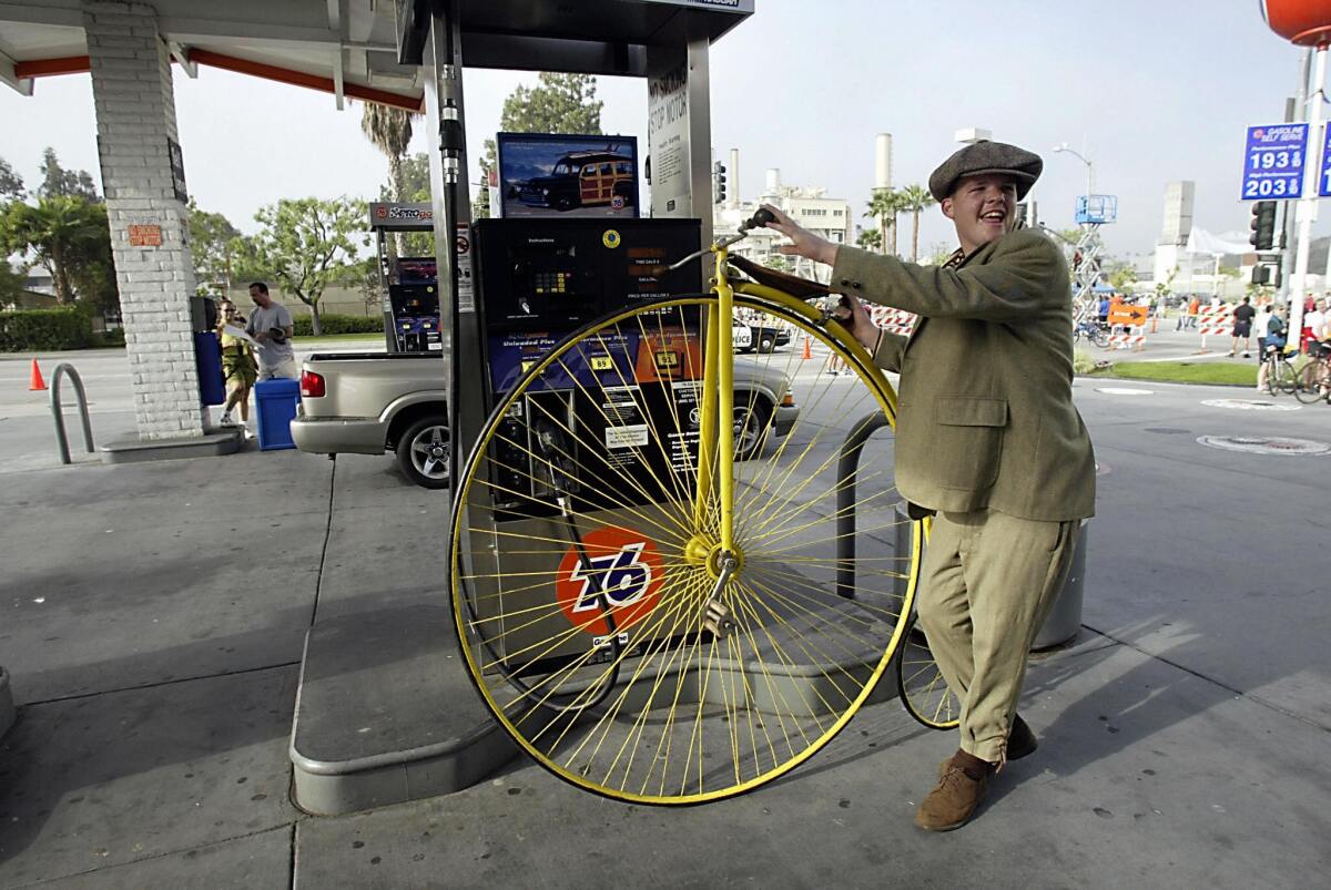 A man in old-fashioned clothes next to a penny-farthing bicycle with a large front wheel and small back wheel