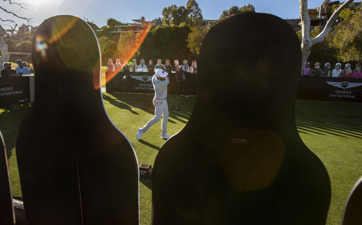 Dustin Johnson hits his tee shot on the par-three 18th in front of cardboard cutout fans on Feb. 19, 2021.