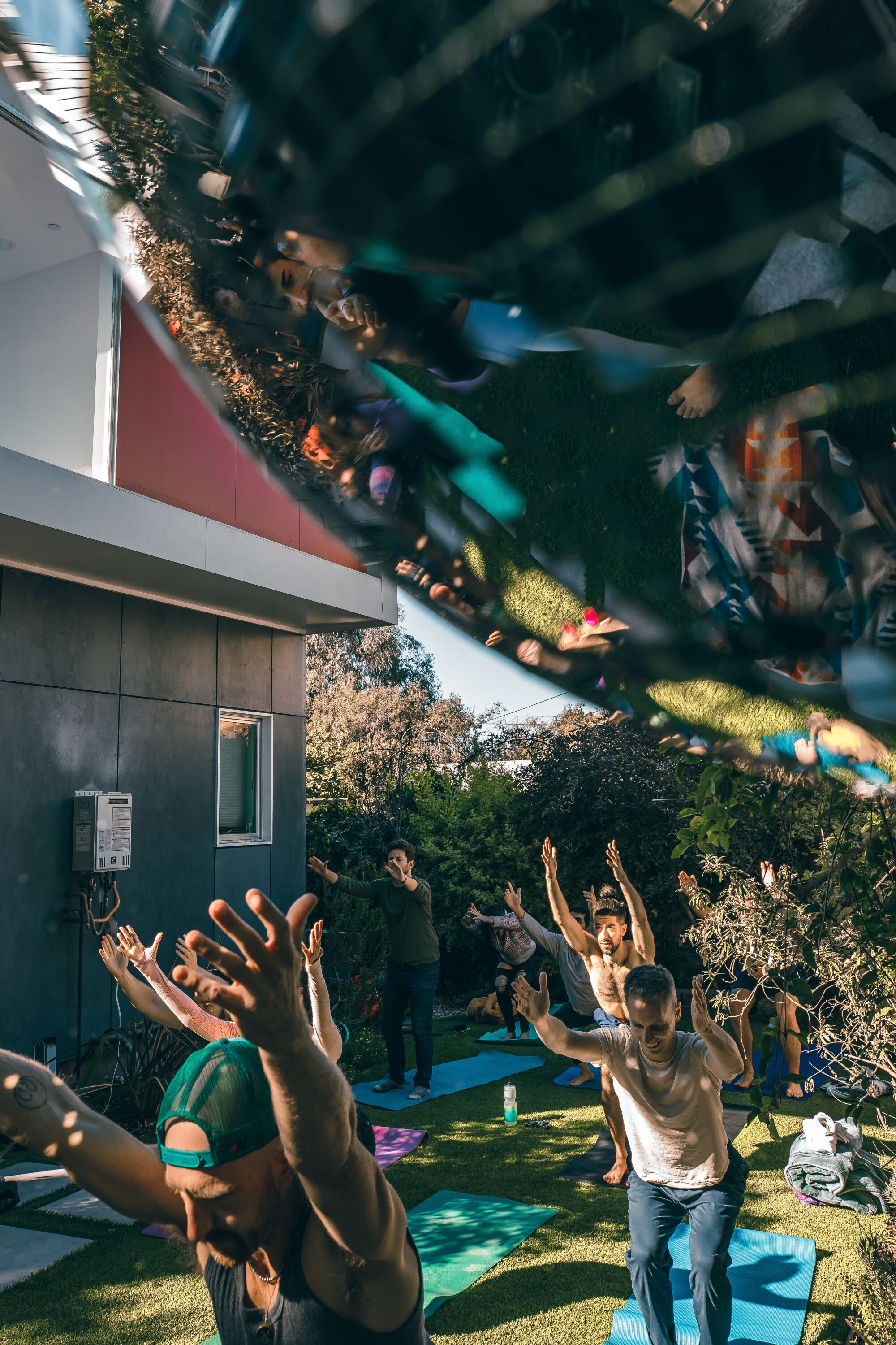 A view of people doing yoga in a backyard, which is reflected in a disco ball at the edge of the frame.