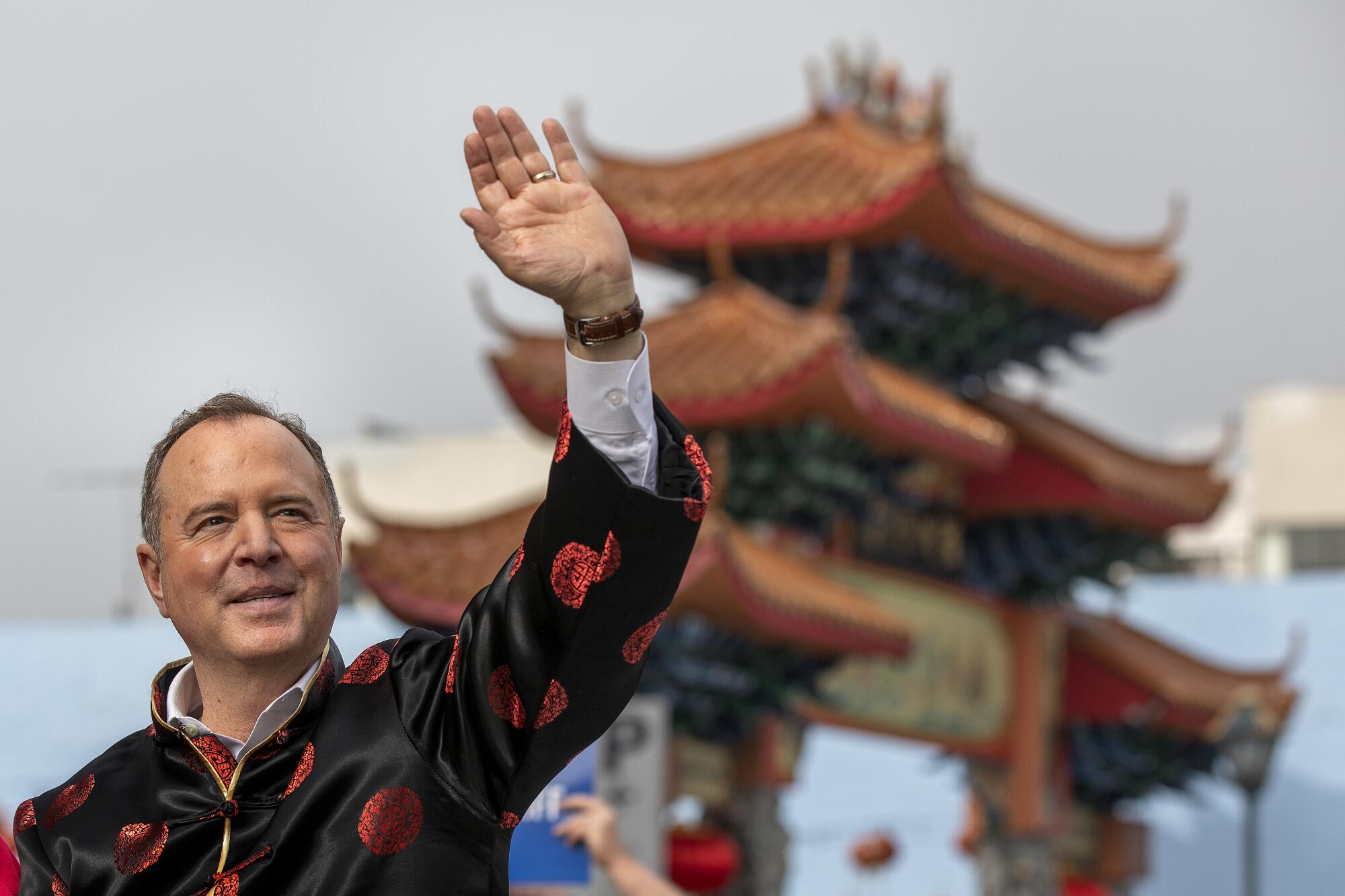 Adam Schiff seen from the chest up in a traditional Chinese jacket, waving, a pagoda in the background