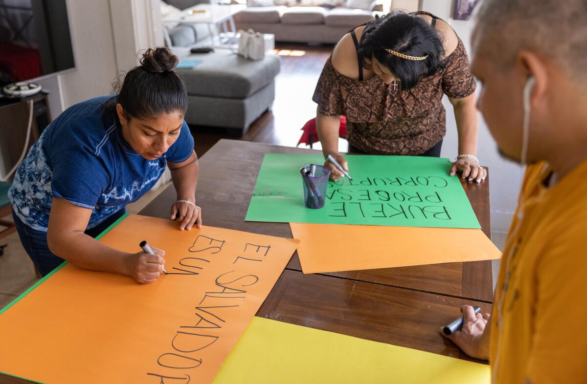 Two women and a man prepare signs using posters and black markers