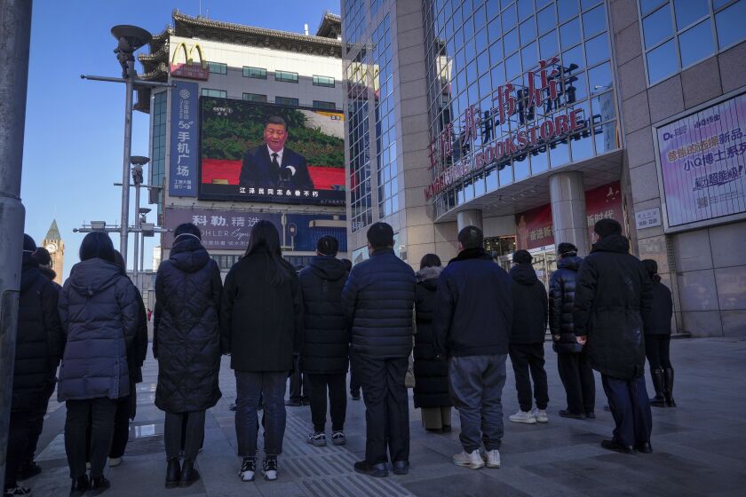People watch a live broadcast of the memorial service for late former Chinese President Jiang Zemin where Chinese President Xi Jinping makes a speech on screen at the Wangfujing shopping street in Beijing, Tuesday, Dec. 6, 2022. A formal memorial service was held Tuesday at the Great Hall of the People, the seat of the ceremonial legislature in the center of Beijing. (AP Photo/Andy Wong)