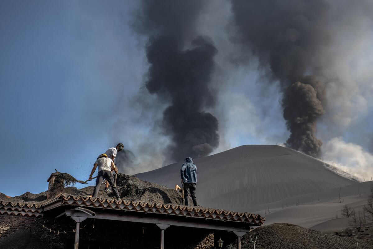 Varias personas limpian la ceniza de un tejado durante la erupción de un volcán en la isla de La Palma, España.