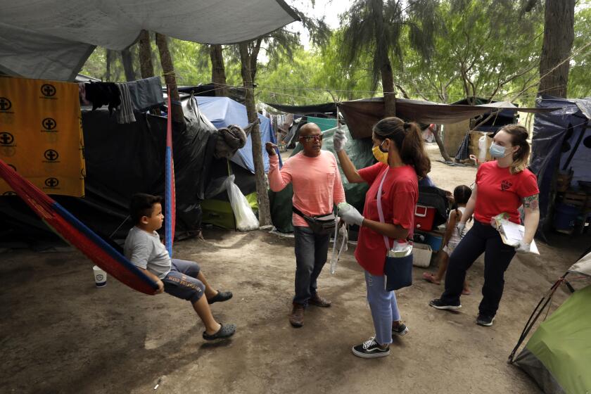 MATAMOROS, MEXICO-MAY 15, 2020-Cuban nurse and asylum seeker Mileydis Tamayo Salgado, 50, second from right, visited tents in the sprawling border camp in Matamoros, Mexico, taking migrants' temperatures with U.S. volunteer Megan Reynolds, 26, right, a registered nurse. They are trying to detect people who have the flu or other coronavirus symptoms. At the Matamoros refugee camp, where hundreds of asylum seekers are waiting under the "Remain in Mexico" program, a group of doctors from Cuba, who are also asylum seekers are helping to take care of camp residents at the non-profit Global Response Management clinic. There has yet to be one case of Covid-19 inside the camp during the pandemic, and they are working hard to keep it that way. (Carolyn Cole/Los Angeles Times)
