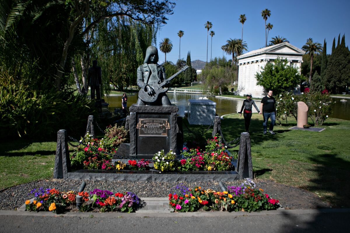 People walk by Johnny Ramone, an American guitarist and songwriter's grave as they visit the Hollywood Forever Cemetery