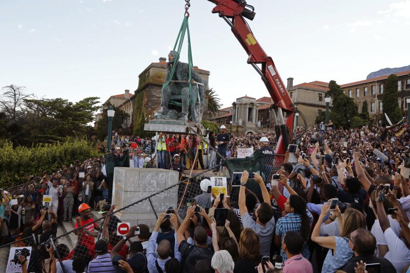 FLE - In this April 9, 2015, file photo, cheering students surround a statue of British colonialist Cecil Rhodes, as it is removed from the campus at the Cape Town University, Cape Town, South Africa. New campaigns in the U.S. and Europe to pull down monuments to slave traders and colonial rulers are now following Africa's lead. (AP Photo/Schalk van Zuydam, File)