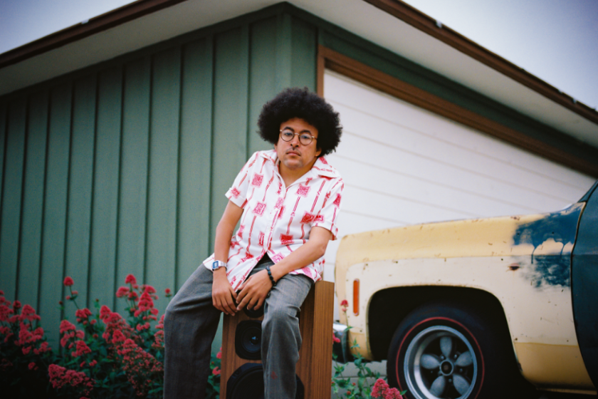 A man sitting on a stereo speaking in front of a vintage car.