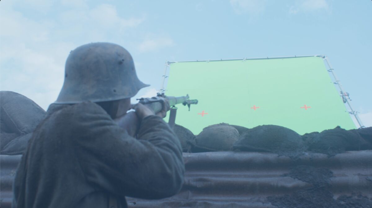 A WWI German soldier fires at a green screen before the VFX team completes the shot in "All Quiet on the Western Front."