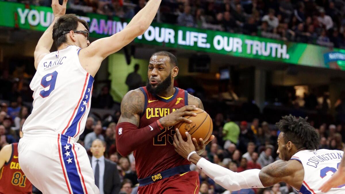 LeBron James drives between Philadelphia 76ers' Dario Saric and Robert Covington during the second half.