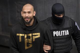 A police officer escorts Andrew Tate, handcuffed, from the Court of Appeal in Bucharest, Romania