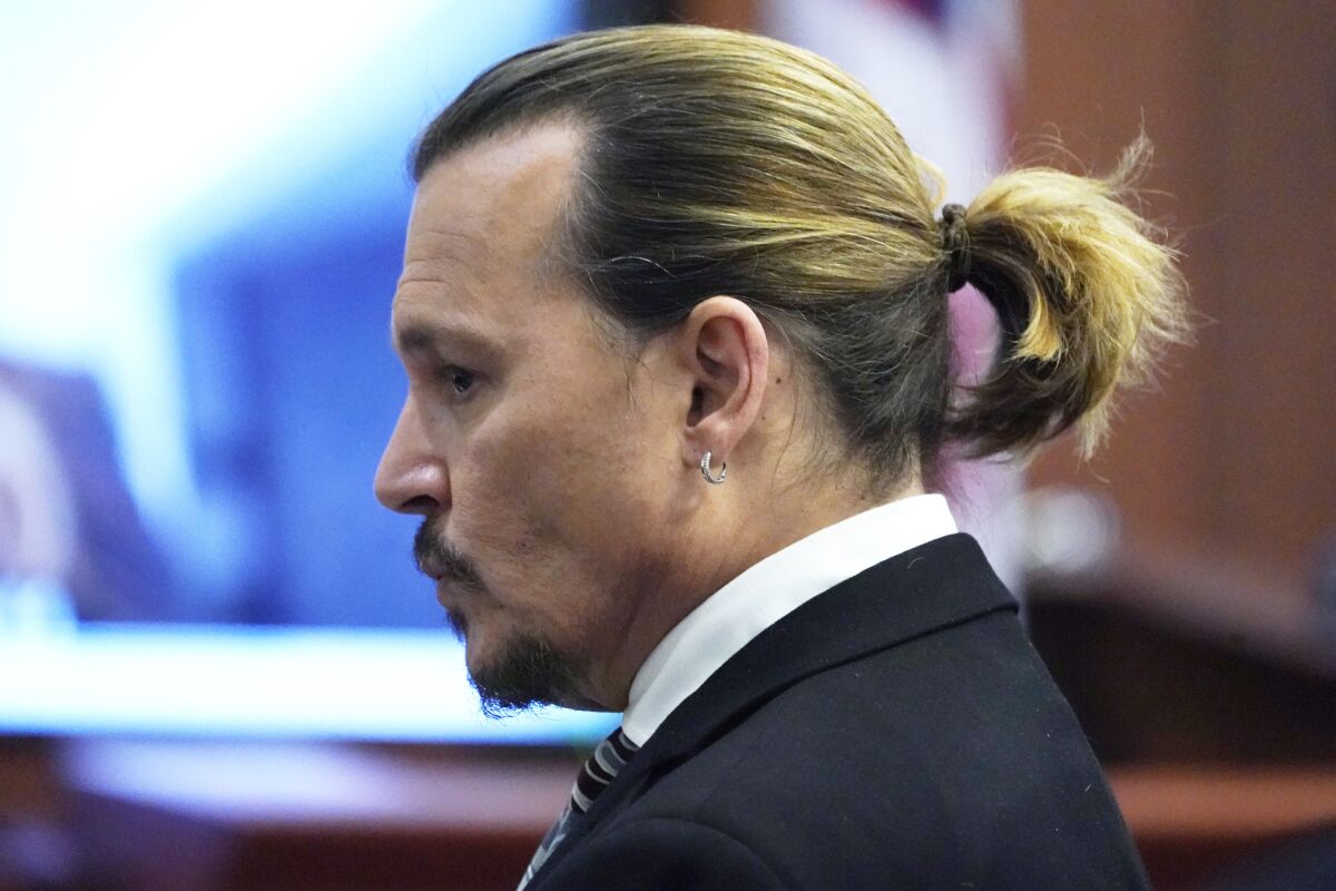 A side view of a man wearing a suit and a small ponytail in a courtroom.