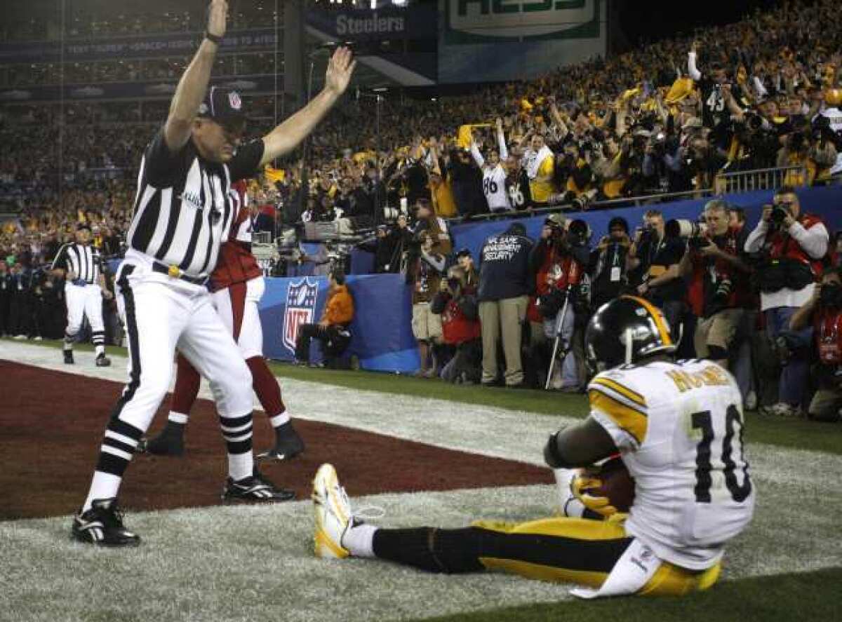 Steelers receiver Santonio Holmes, sitting in the end zone as the referee signals, clutches the football after making a game-winning touchdown catch against the Cardinals in Super Bowl XLIV.