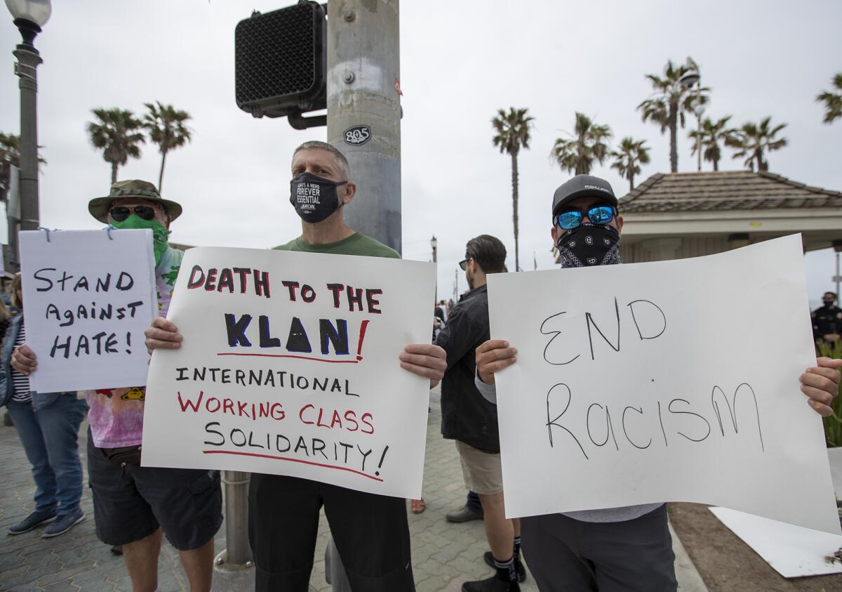 Nick McLachlan, Cliff Smith and Gesus Portilla hold signs during an antiracism rally in Huntington Beach.