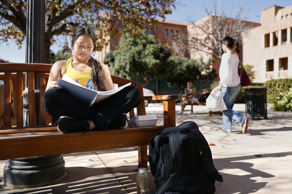 加州大学洛杉矶分校青少年体操运动员艾玛·马拉布约 (Emma Malabuyo) 坐在棕熊队校园的户外长凳上准备期中考试。