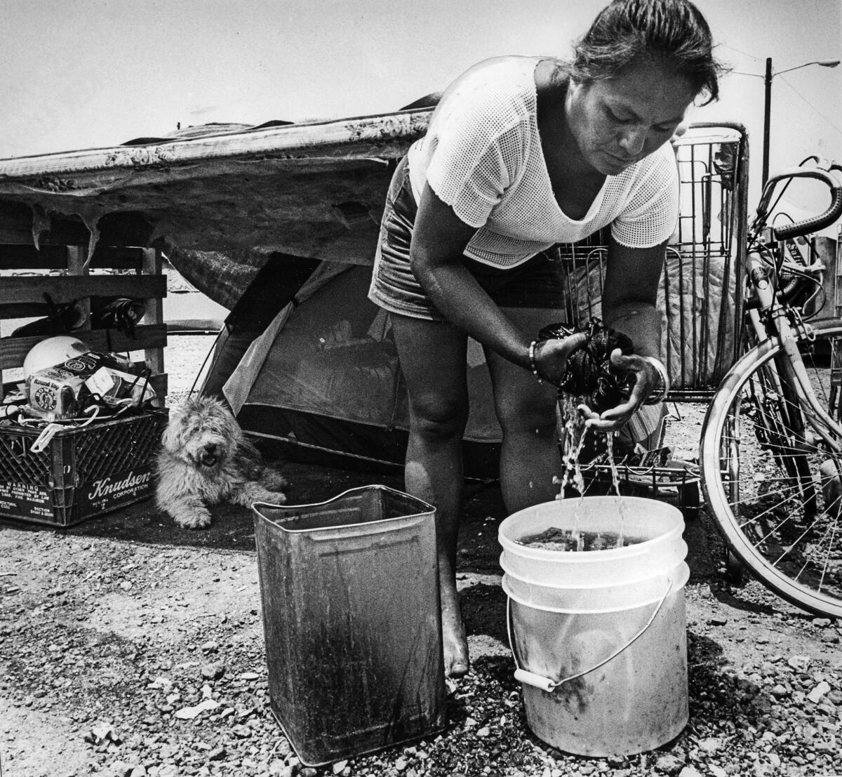 June 26, 1987: Esperanza Huerta washes clothes in front of tent while her dog Snowball takes it easy in the shade.
