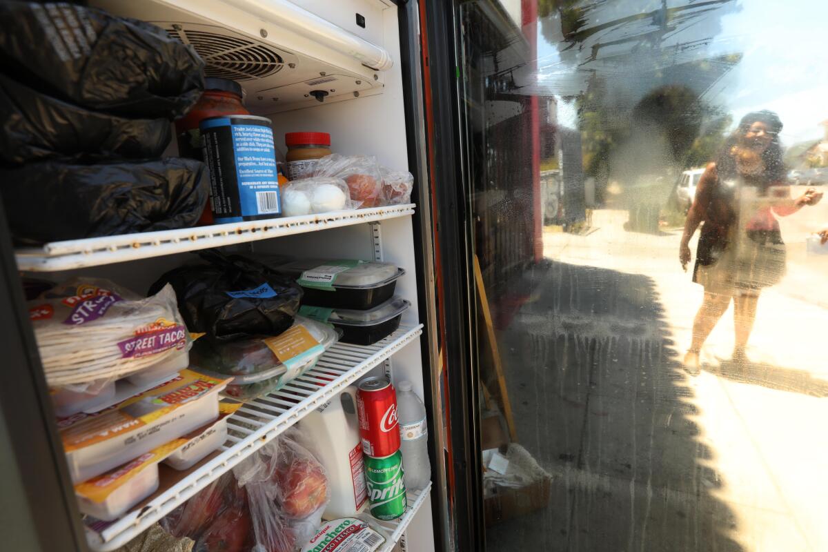 Artist Mary A. Harris is seen through the door of a refrigerator containing donated food at Little Amsterdam coffee shop.