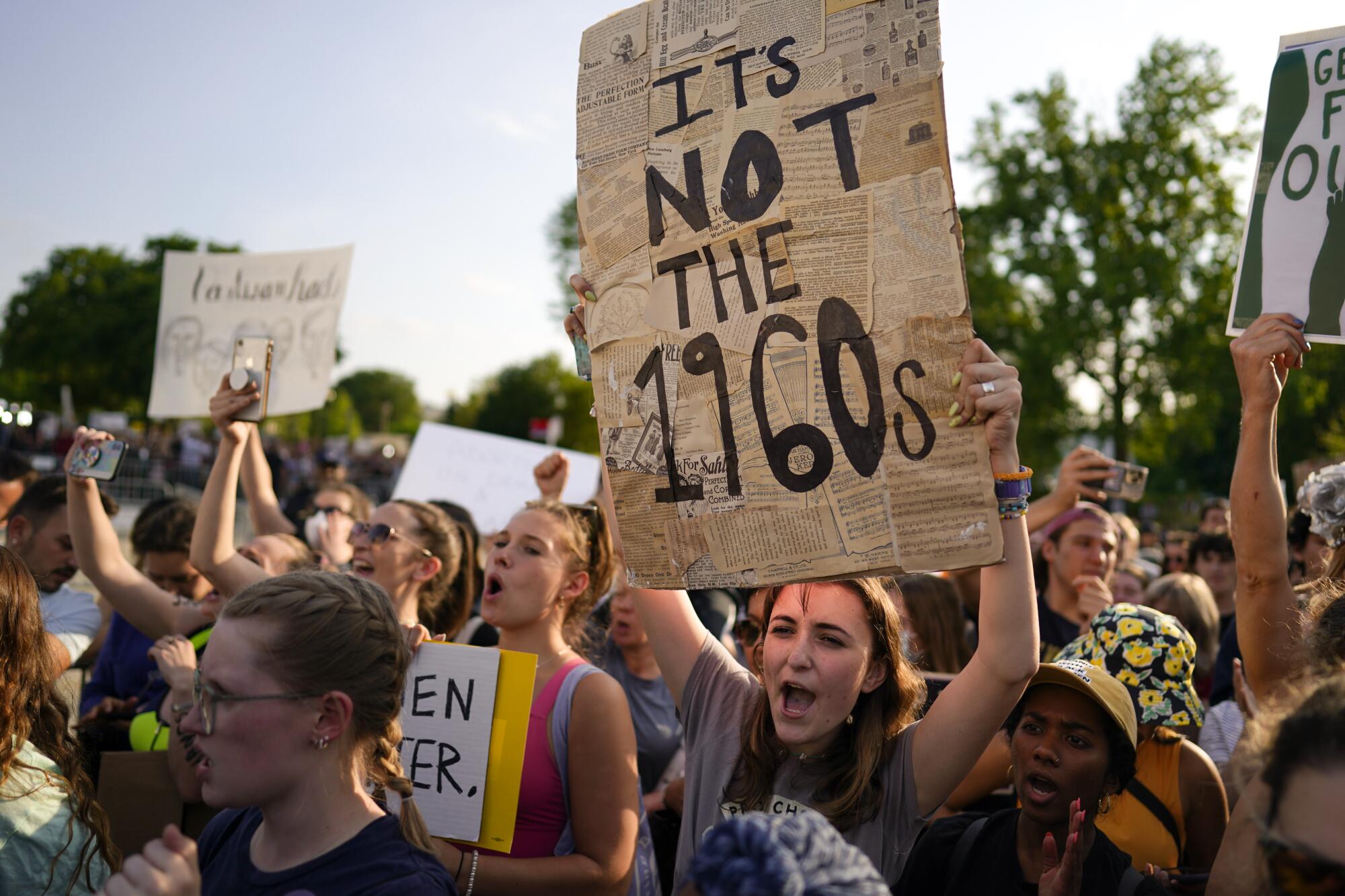 A crowd of protesters, one holding a sign that reads, "It's not the 1960s."