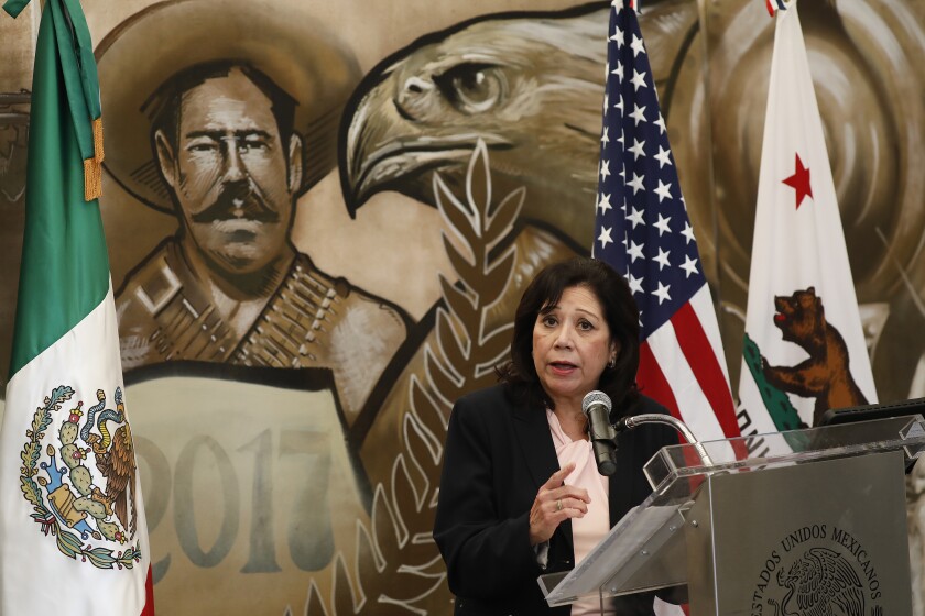 A person stands at a lectern in front of U.S., California and Mexican flags.