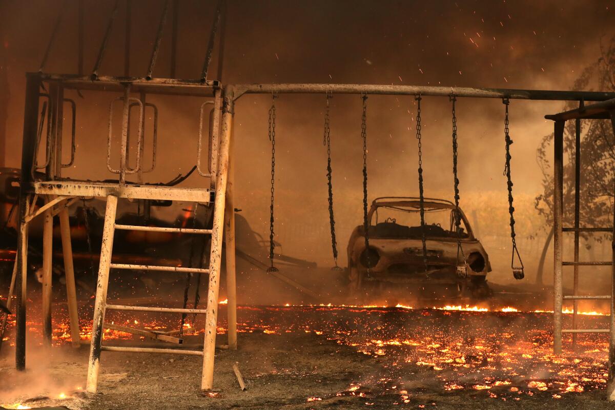 A burned car and swing set are surrounded by embers from the Kincade fire on Thursday in Geyserville, Calif.