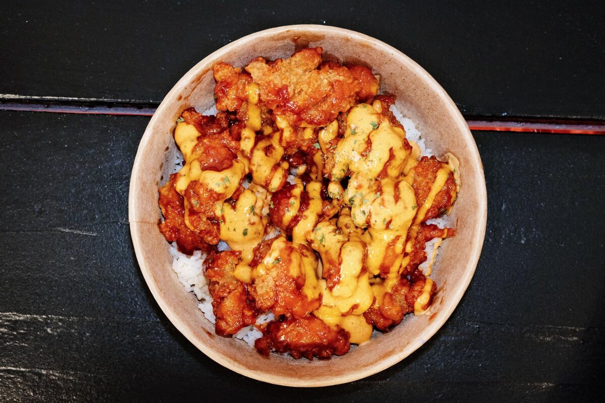 Korean fried chicken on rice in a bowl, drizzled with a yellow sauce 