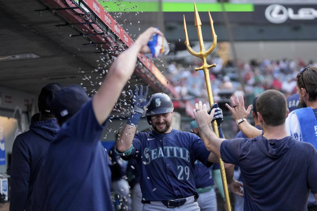 Cal Raleigh holds a prop trident in the dugout as Mariners celebrate his third-inning home run at Angel Stadium