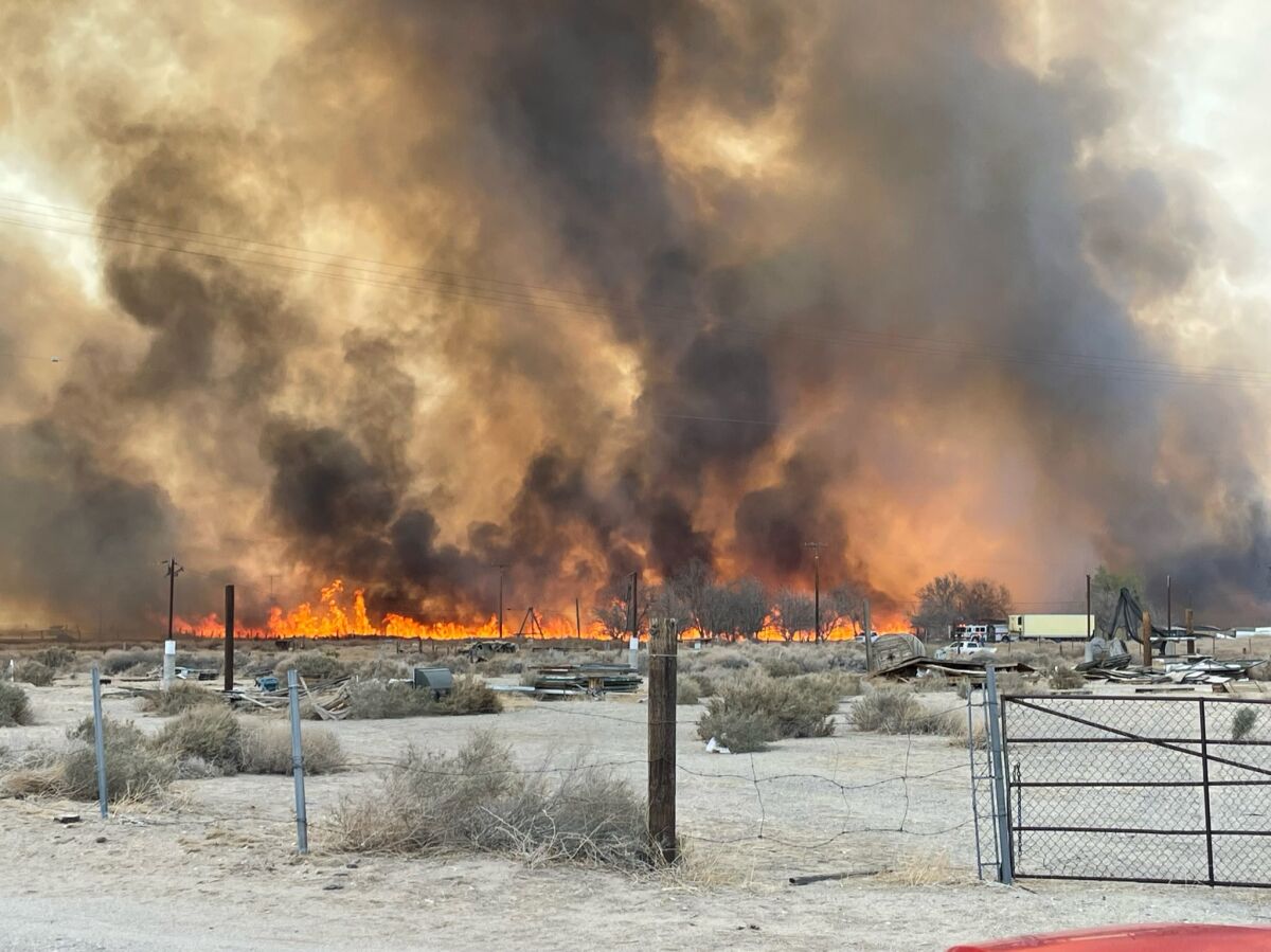 Flames and black smoke rise from a rural area in the high desert