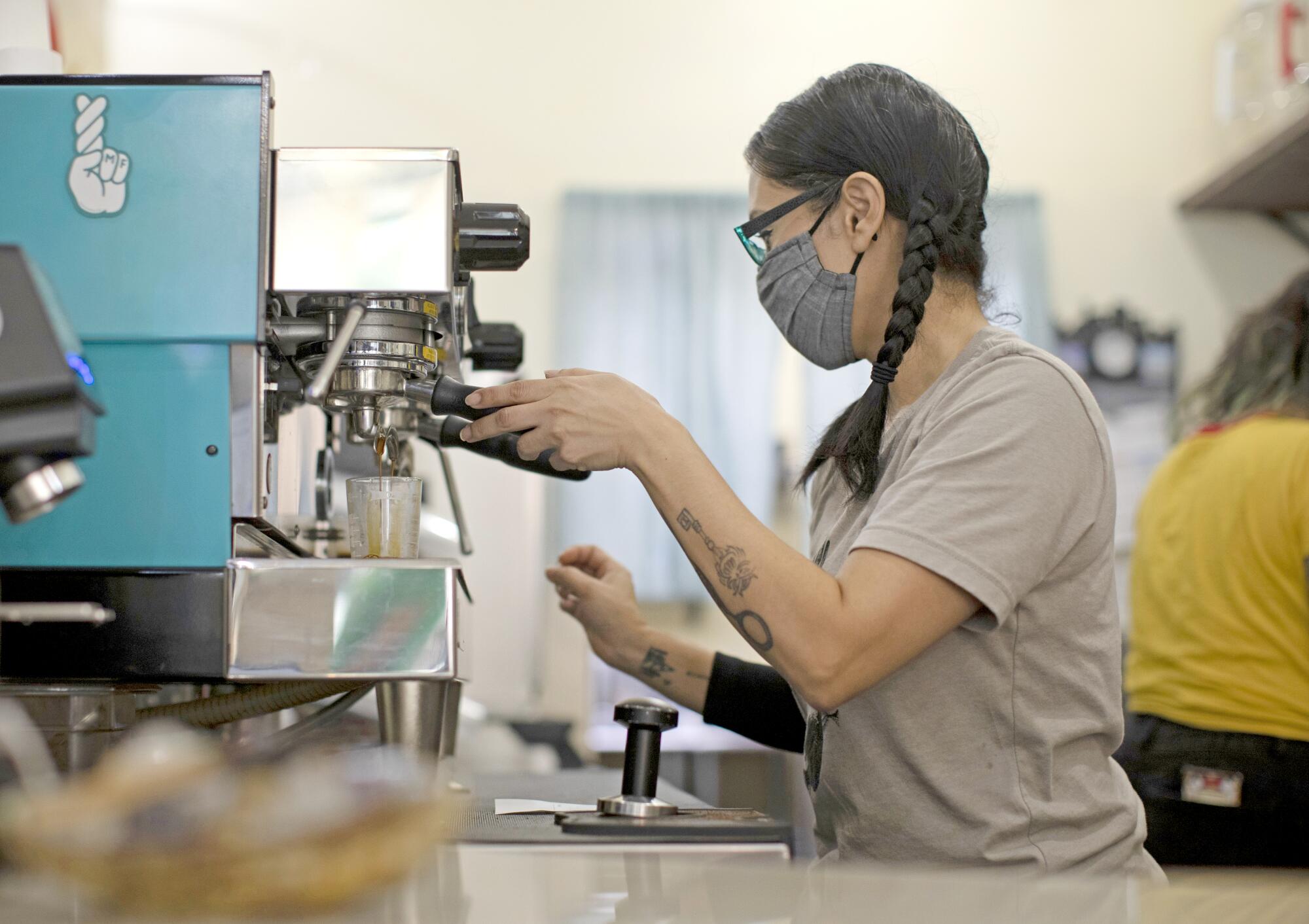 A woman makes a drink at an espresso machine.