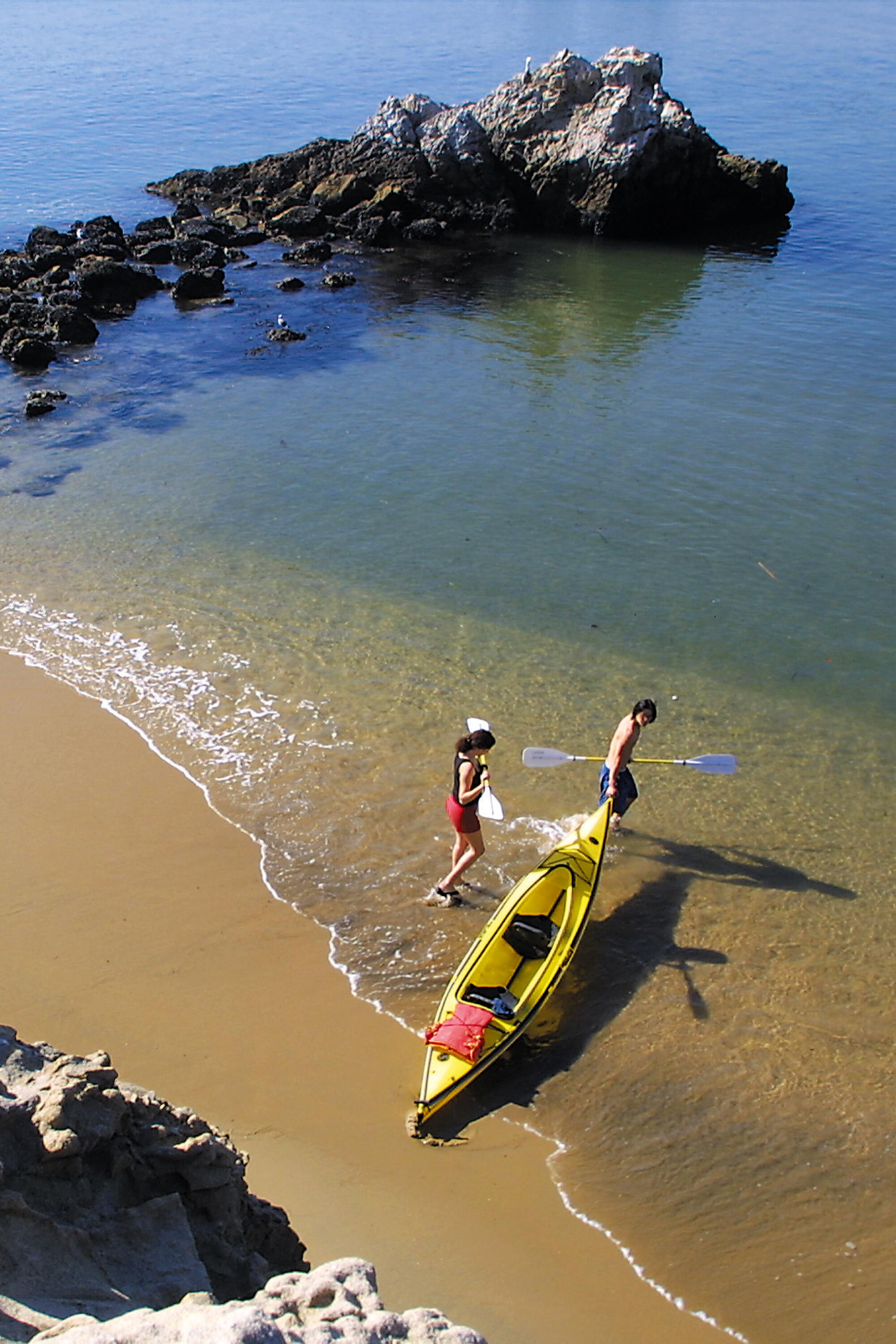 Two people pull a yellow kayak into the water.