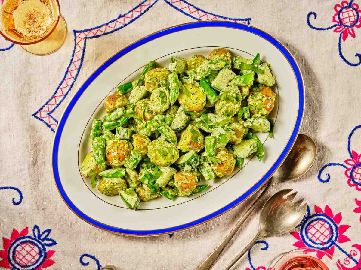 Green Potato Salad with Zhoug on a blue-rimmed white oval platter, sitting on a colorful tablecloth.