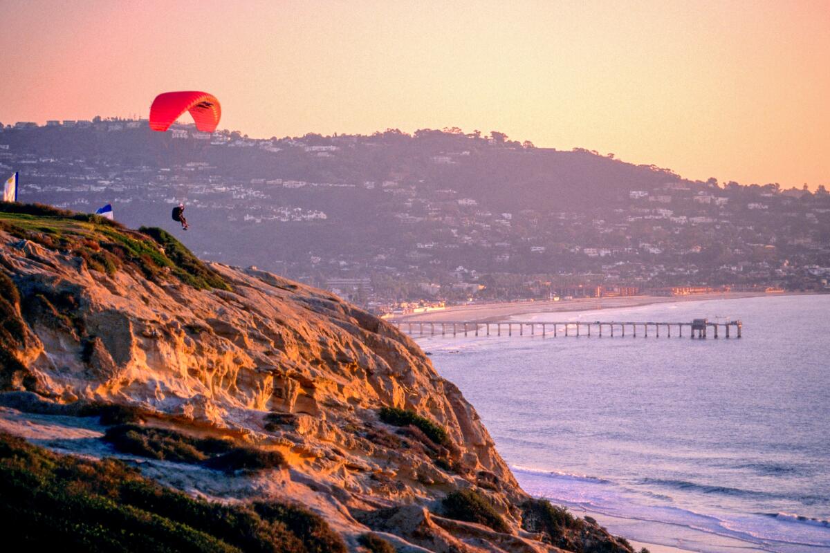 A person on a hang glider soars over the cliffs of San Diego