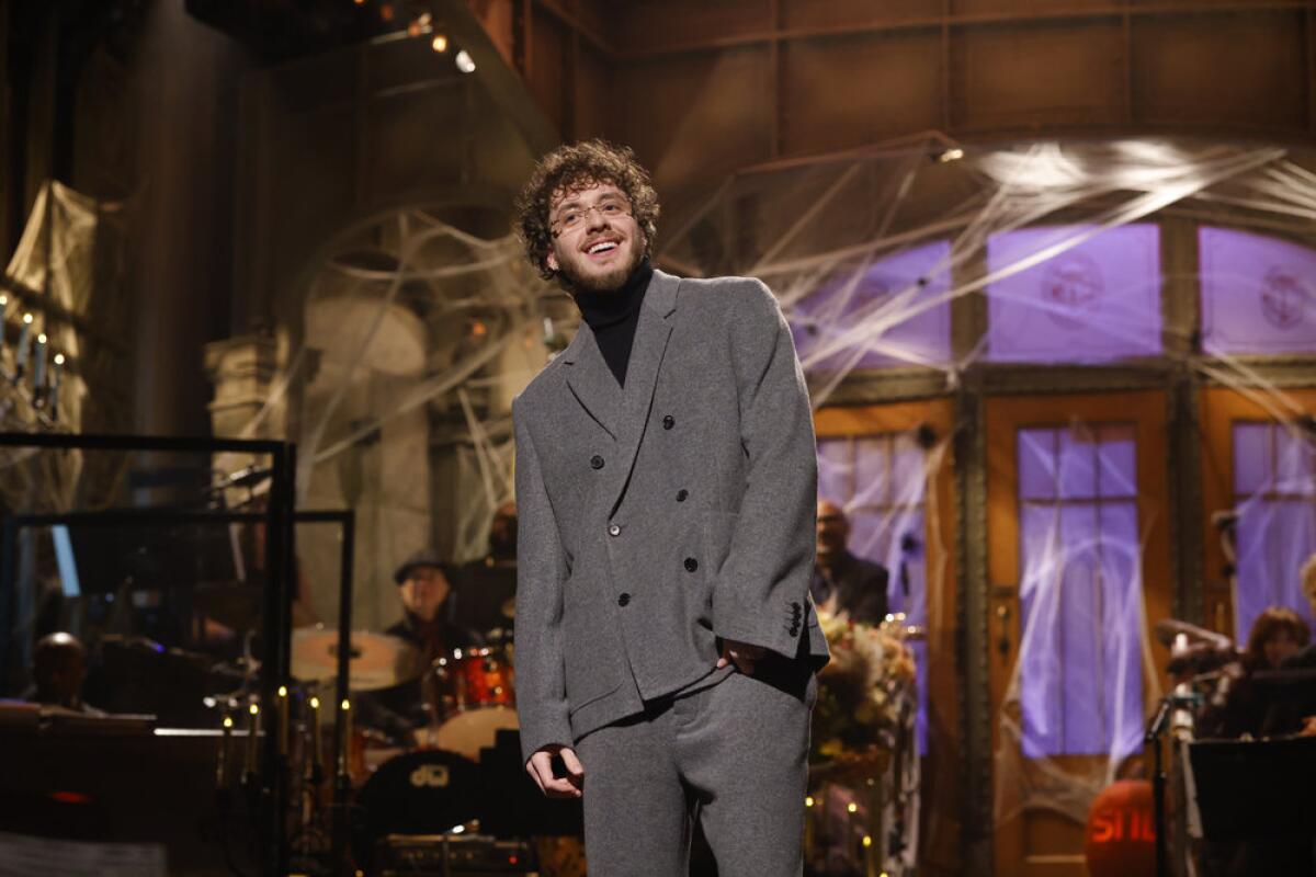 A man with curly blond hair smiling in a gray suit on a stage