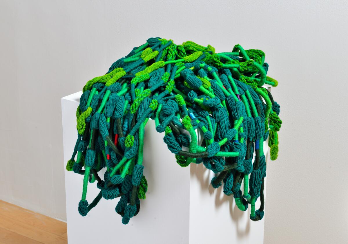 Heaps of green wool yarn are displayed on a white pedestal.