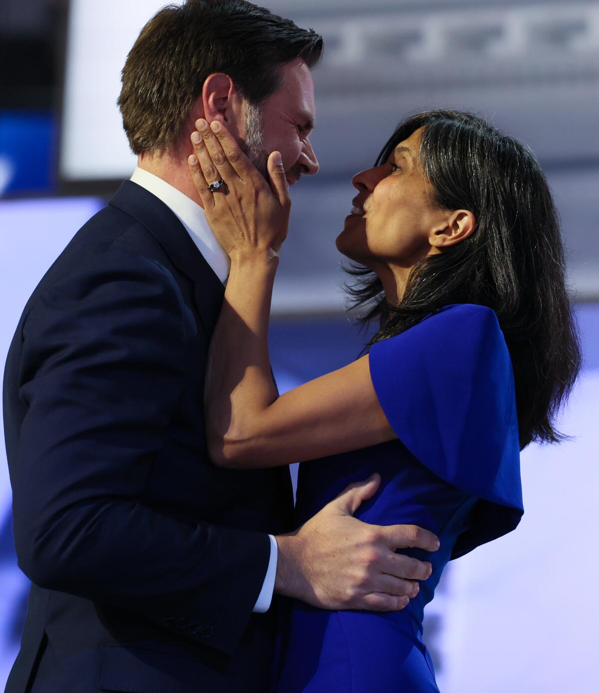 A man with dark hair, left, in a dark suit embraces a woman with dark hair, in a purple dress 