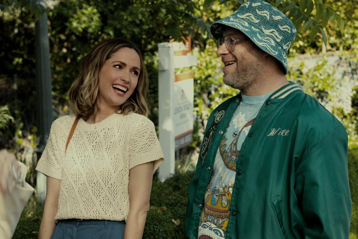 A man and a woman stand outdoors together laughing.