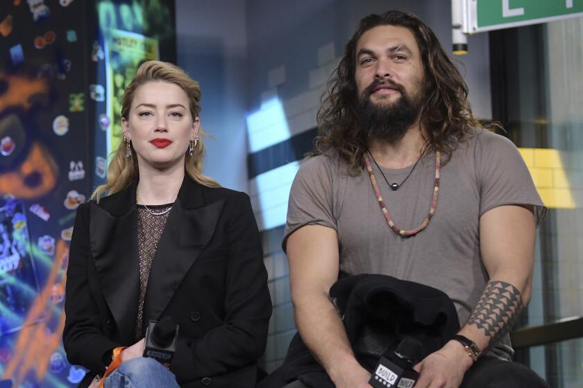 A blond woman and a large bearded man hold microphones while sitting and waiting to answer questions