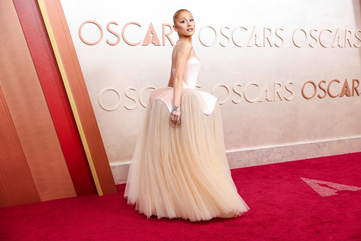 An actor in a fancy gown walks on a red carpet at an awards show.