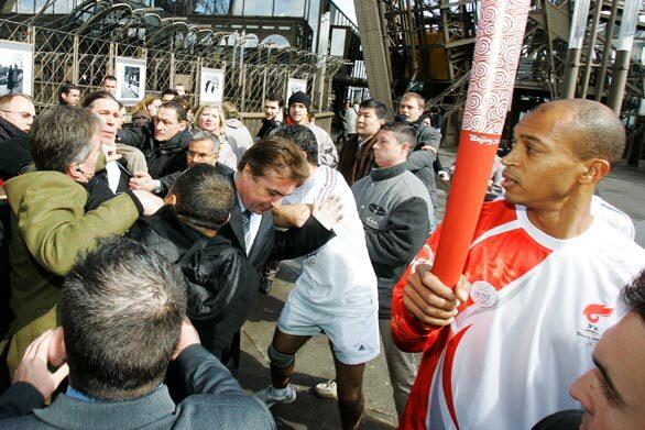 Security officers grab Green Party activist Sylvain Garel, third left at rear, as he tries to approach Olympic torchbearer Stephane Diagana, right, the 1997 400-meter world champion. Because of heavy protests during the Paris torch relay, security officials had to extinguish the torch and carry it aboard a bus at various points.
