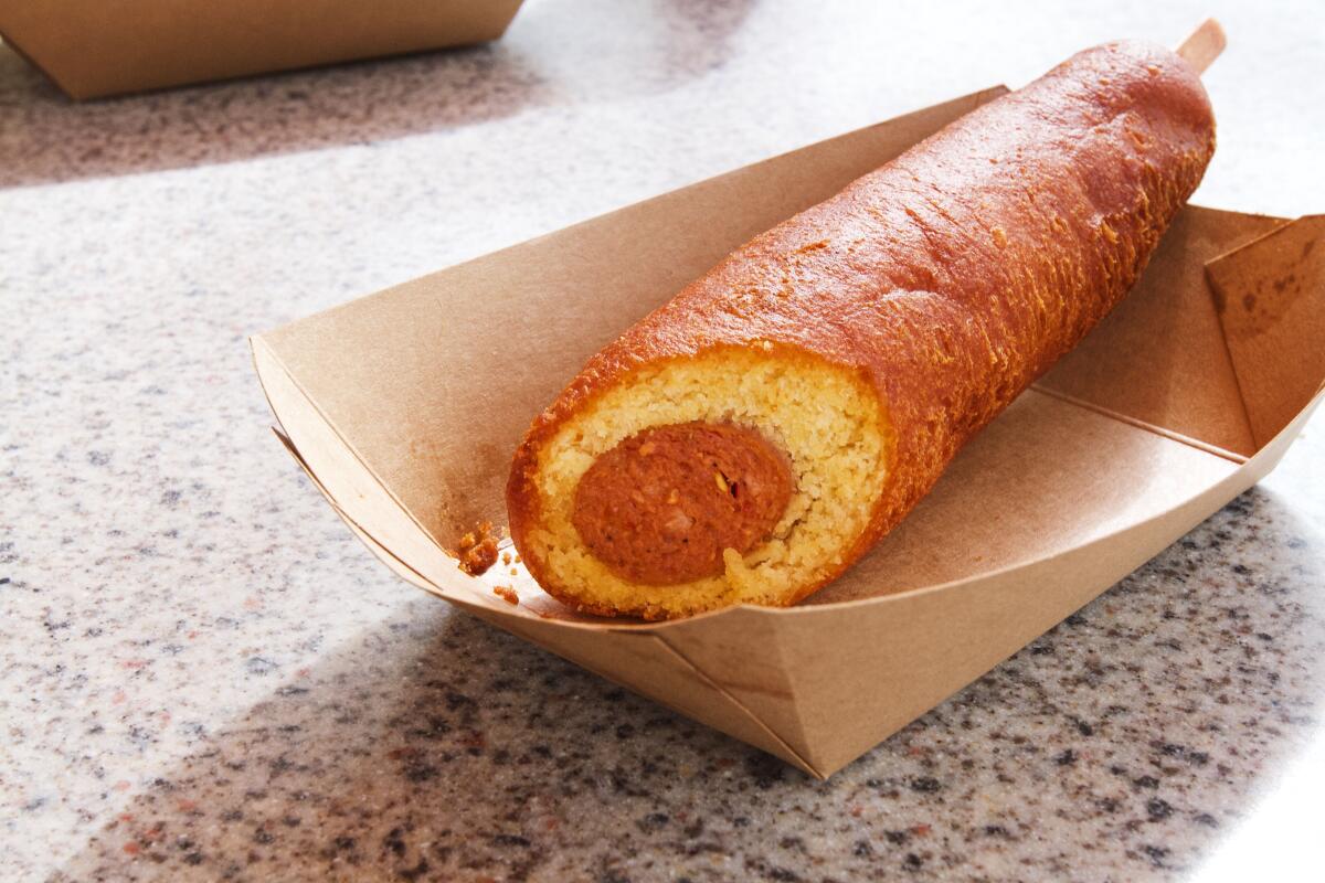 A photo of a hot link corn dog, its top cut off to show the sausage, in a cardboard tray