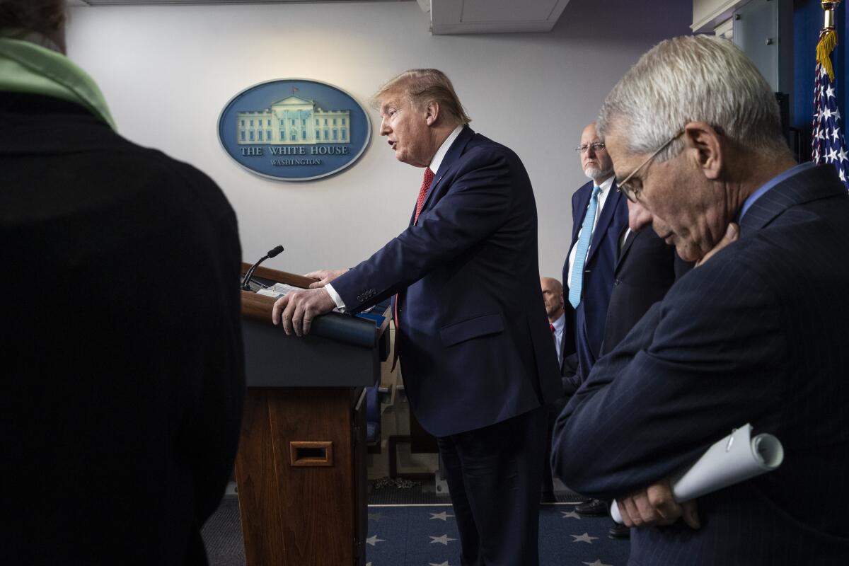 Anthony Fauci looks at the ground as then-President Trump speaks at a news conference.