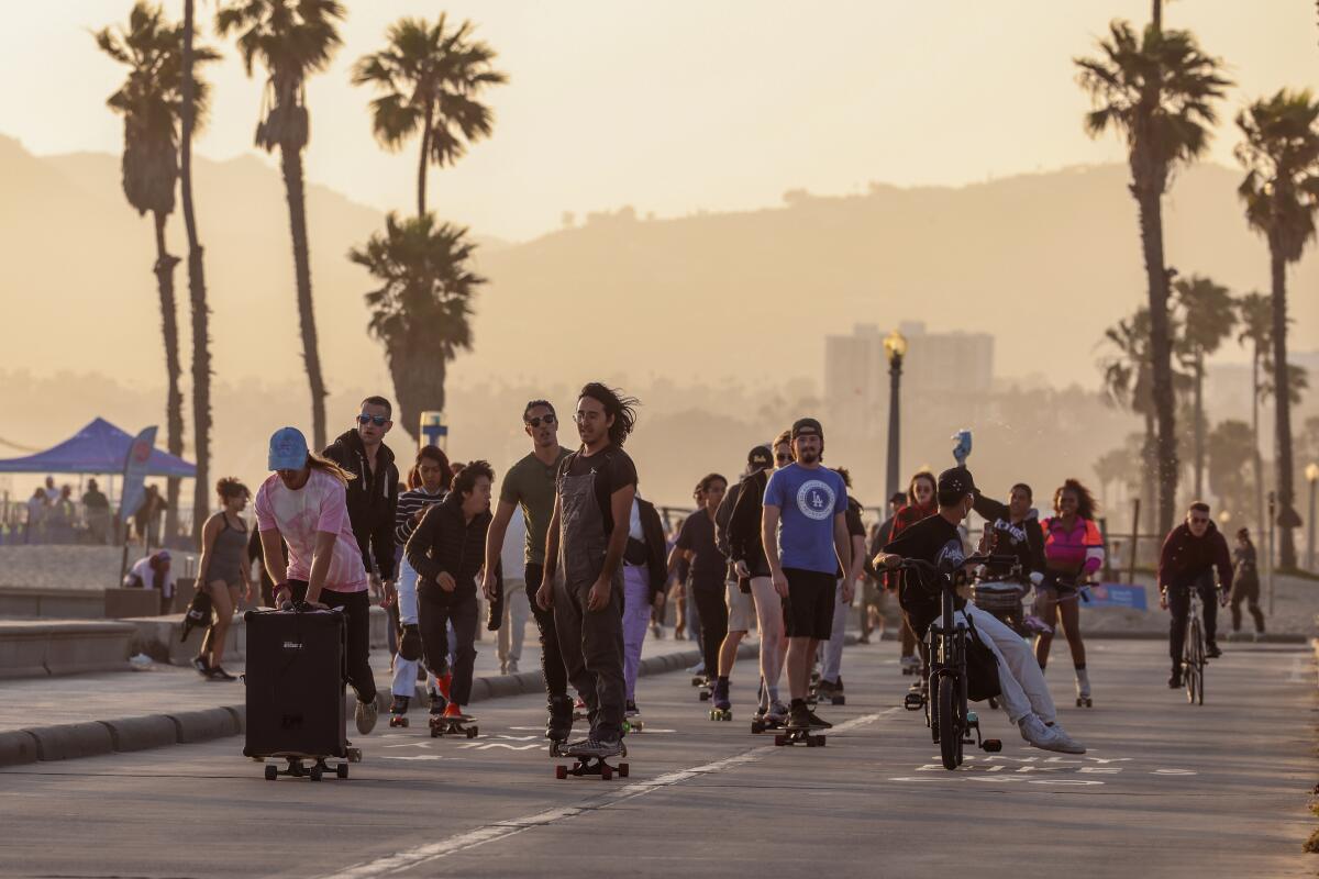 A group of mostly skateboarders ride along the boardwalk at dusk.
