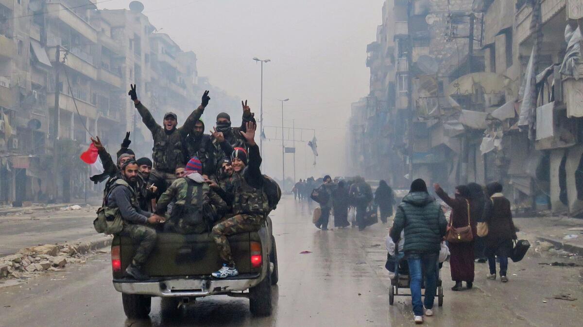 Pro-government fighters drive past residents fleeing violence in Aleppo, Syria, on Dec. 13.