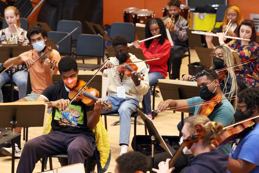 Youth orchestra members, wearing masks, rehearse in a practice room.