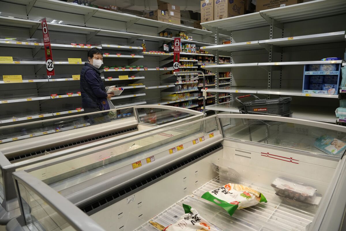A woman walks past empty shelves and freezers as residents concerned with possible shortages, stock up on food at a supermarket in Hong Kong, Thursday, March 3, 2022. As COVID cases continue to rise, health authorities said the government could implement measures that may involve "asking people to stay at home," and that it remains to be seen whether it would be done via legislation or other means. (AP Photo/Vincent Yu)