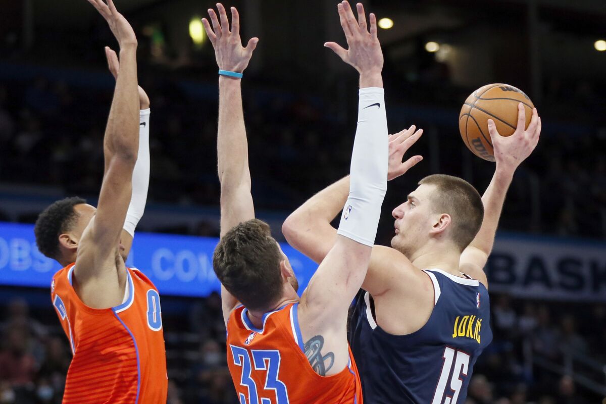 Denver Nuggets center Nikola Jokic, right, passes away from Oklahoma City Thunder forward Darius Bazley, left, and center Mike Muscala, middle, in the first half of an NBA basketball game Sunday, Jan. 9, 2022, in Oklahoma City. (AP Photo/Nate Billings)