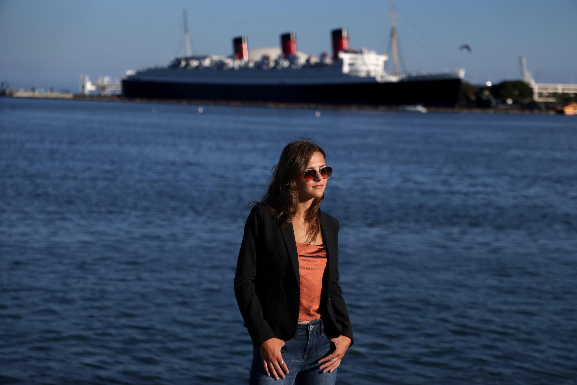 A young woman stands near the Queen Mary in Long Beach.