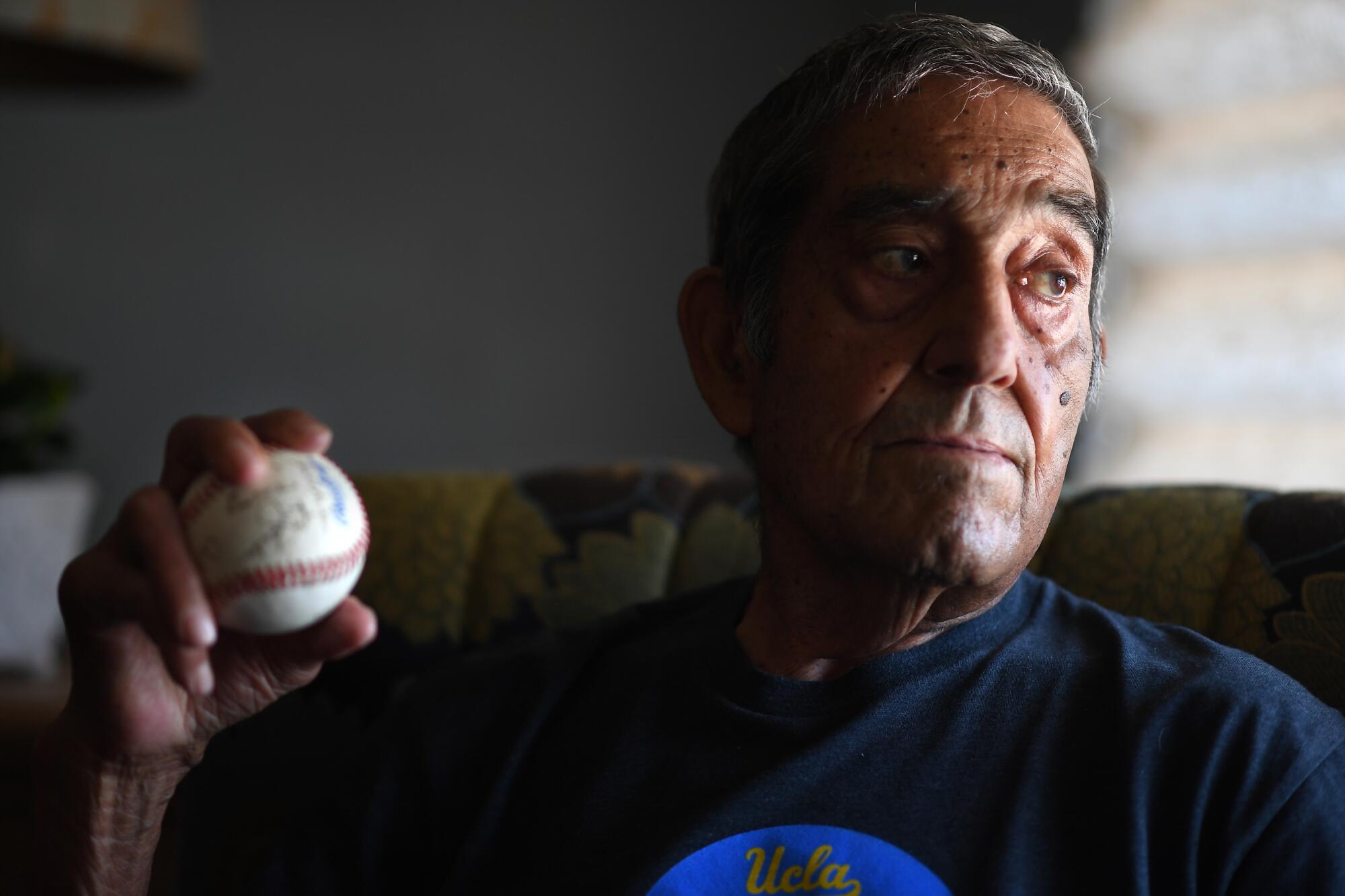 Art Velarde holds an autographed baseball from his living teammates at his home in Hacienda Heights. 