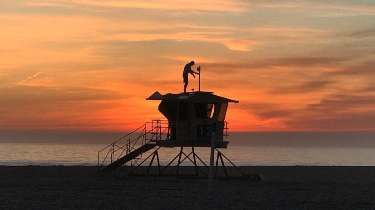 Man atop lifeguard tower silhouetted by sunset
