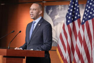 A man speaks at a lectern, with two American flags behind him.